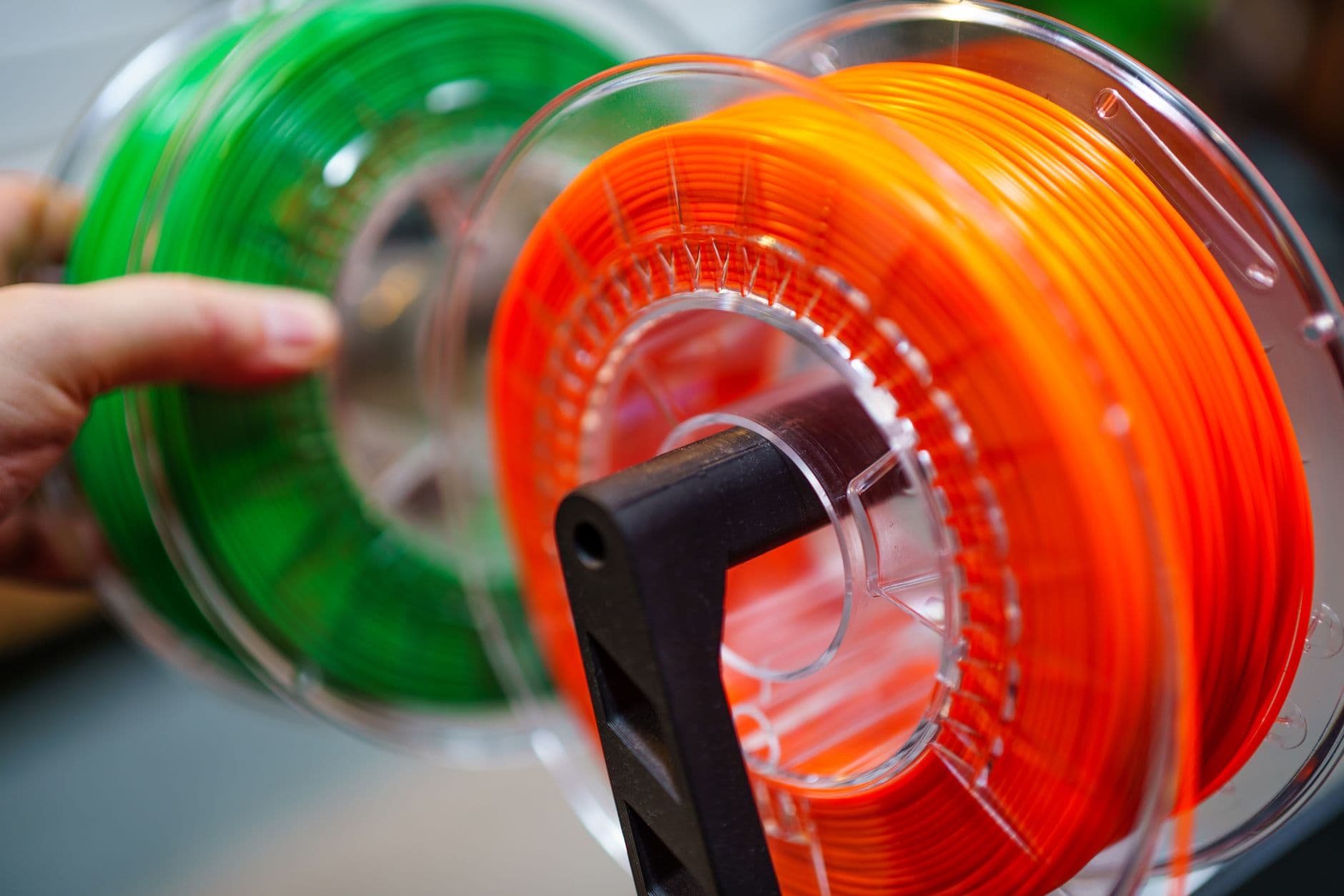 Spools of bright orange and green 3D printer filament on a spool holder