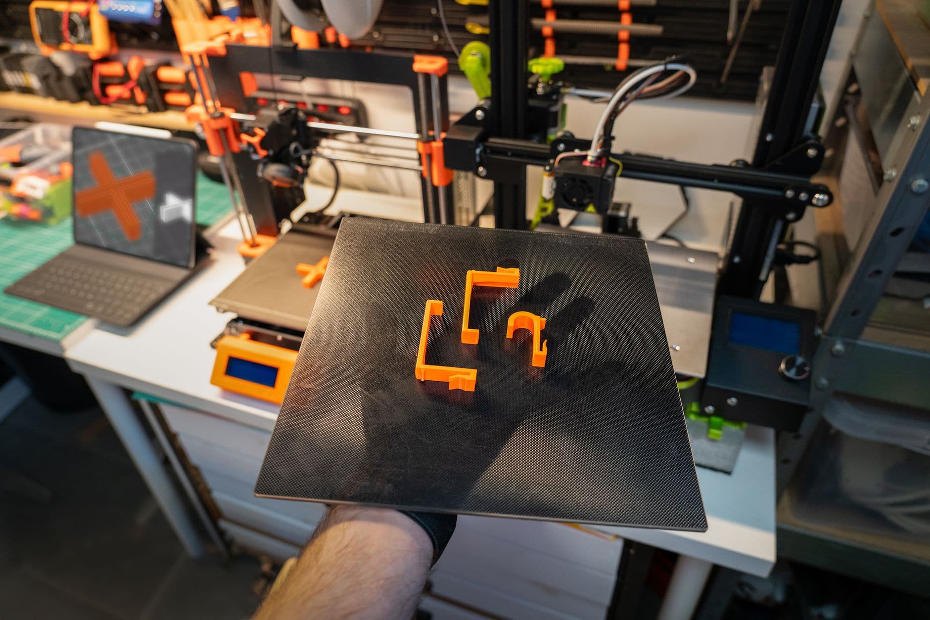 Freshly printed orange parts on a flexible build plate held in front of a 3D printer