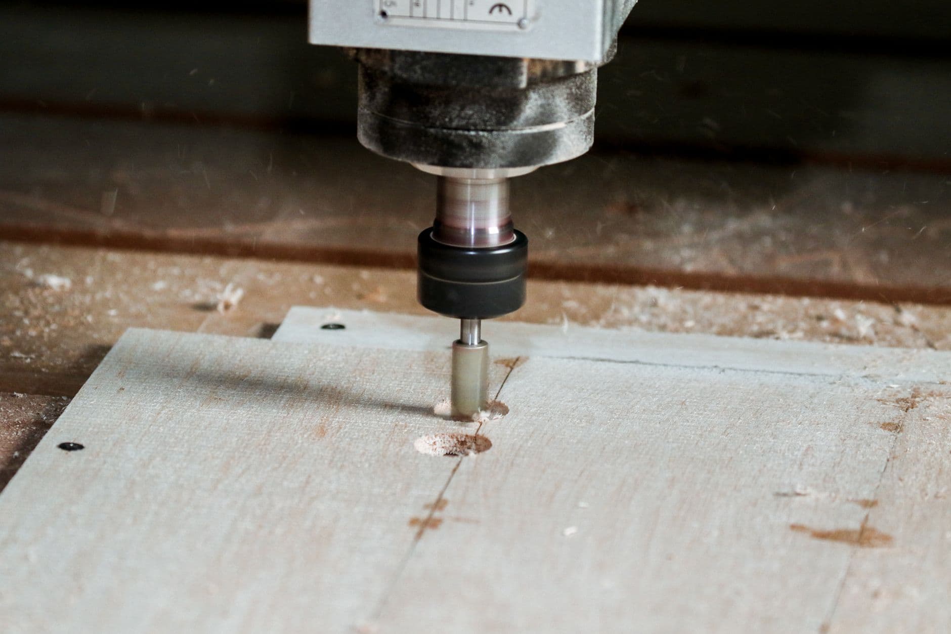 A CNC router spindle boring a hole into a sheet of plywood, wood chips around the cut
