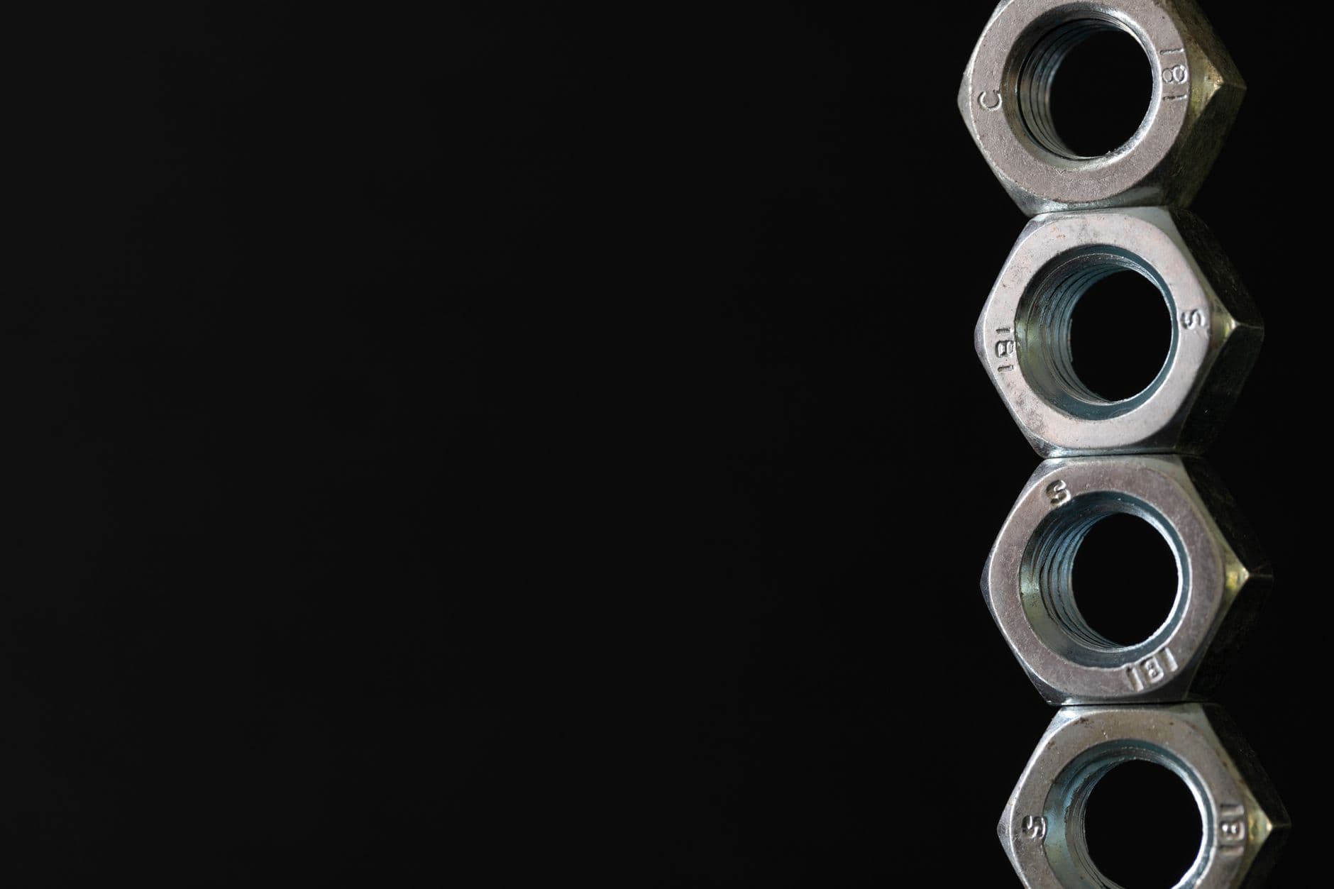 Four zinc-plated hex nuts stacked in a column against a black background